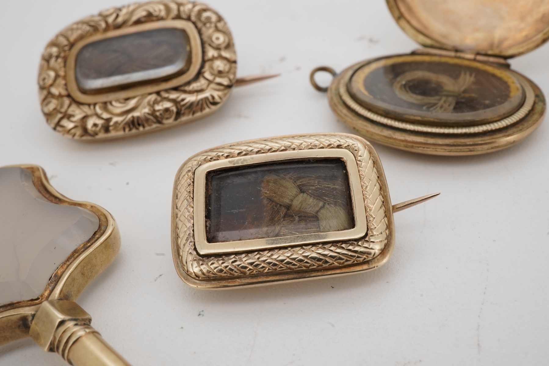 A locket, a watch key and two mourning brooches, the oval locket engraved with foliate details, opening to reveal a glazed panel of hairwork; together with two early 19th century mourning brooches, engraved with flowers